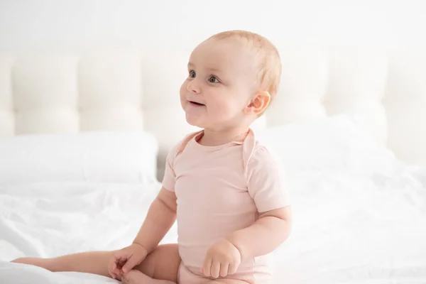 Портрет малышки 10 месяцев в светло-розовом купальнике на белом постельном белье на кровати — стоковое фото