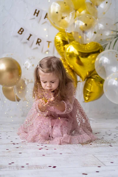 Menina feliz com cabelos longos no vestido rosa soprando confete e celebrando seu aniversário — Fotografia de Stock