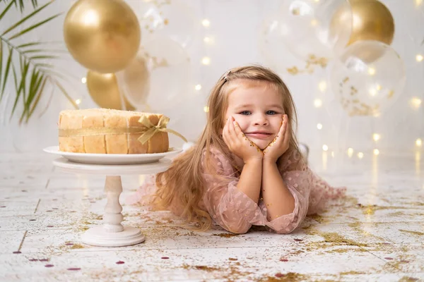 Мила маленька дівчинка лежить на підлозі біля торта на день народження, посміхається, святкує день народження — стокове фото