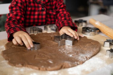 Kırmızı pijamalı küçük bir kız Noel süslü mutfakta zencefilli ekmek pişiriyor. Noel kurabiyeleri