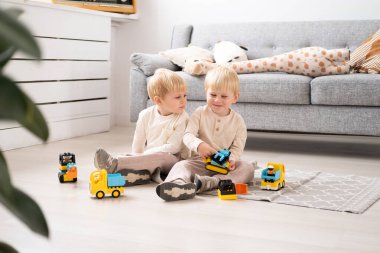 İki komik erkek kardeş ikiz kardeş oyuncak araba yapımcısıyla oturma odasında oynuyor.