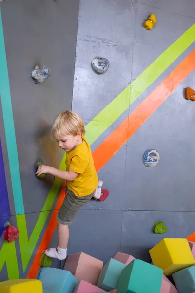 Mały uroczy chłopiec wspina się na pionową ścianę wewnątrz parku rozrywki — Zdjęcie stockowe