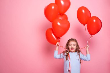 Kırmızı kalpli güzel bir kız çocuğu pembe arka planda romantik balonlar. Sevgililer Günü Konsepti