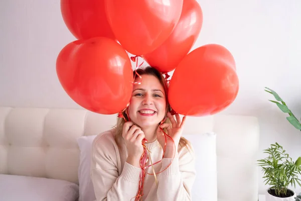 Mulheres bonitas em roupas aconchegantes casuais na cama com balões de coração vermelho, celebrando o dia dos namorados — Fotografia de Stock
