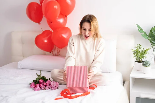 Mulheres bonitas em roupas aconchegantes casuais com caixa de presente e balões na cama celebrando o dia dos namorados — Fotografia de Stock