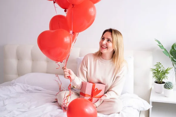 Mulheres bonitas em roupas aconchegantes casuais na cama com balões de coração vermelho, celebrando o dia dos namorados — Fotografia de Stock