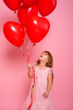 Pembe elbiseli, pembe arka planda kırmızı kalp balonları olan sevimli bir kız çocuğu. Sevgililer Günü