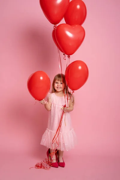 Мила дівчинка в рожевій сукні з червоними кулями серця на рожевому фоні. День святого Валентина — стокове фото
