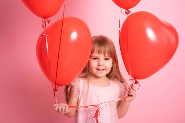 Mignonne fille enfant en robe rose avec des ballons coeur rouge sur fond rose. Saint Valentin — Photo