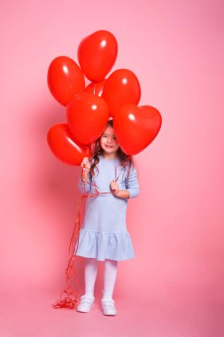 Kırmızı kalpli güzel bir kız çocuğu pembe arka planda romantik balonlar. Sevgililer Günü kavramı