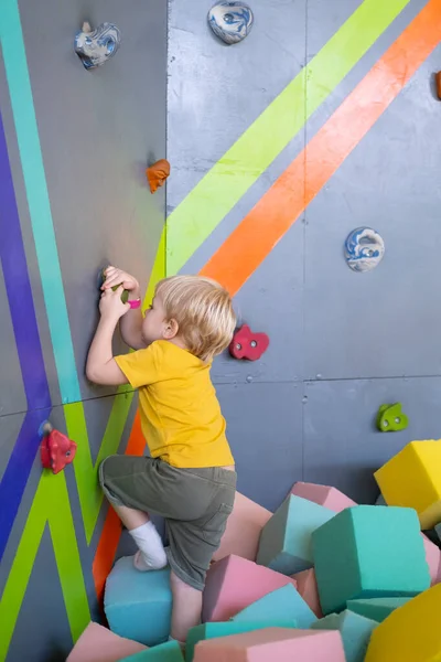 Mały uroczy chłopiec wspina się na pionową ścianę wewnątrz parku rozrywki — Zdjęcie stockowe