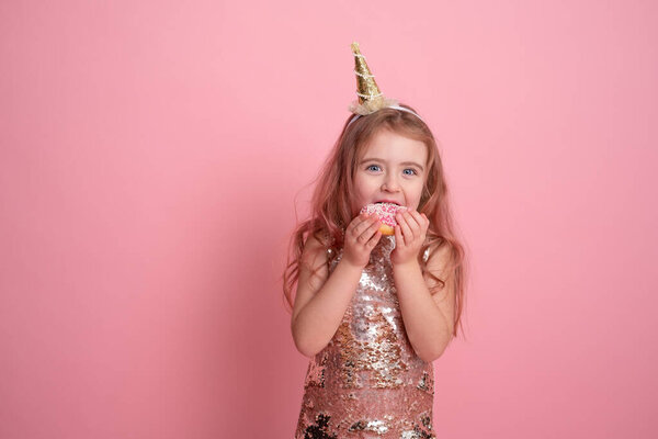 Смешная девочка в блестках платье в праздничной кепке едят пончики на розовом фоне