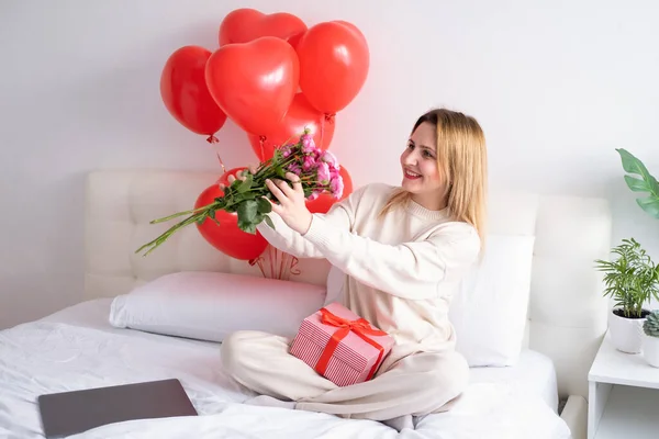 Hermosas mujeres sosteniendo ramo de rosas rosadas en la cama celebrando el día de San Valentín Imagen De Stock