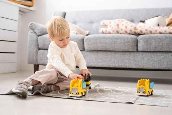 Смешной мальчик играет с конструктором игрушечных машин в гостиной — стоковое фото