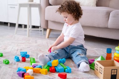 Kıvırcık kız piramit ve inşaatçıyla evde oynuyor. Erken çocuk gelişimi