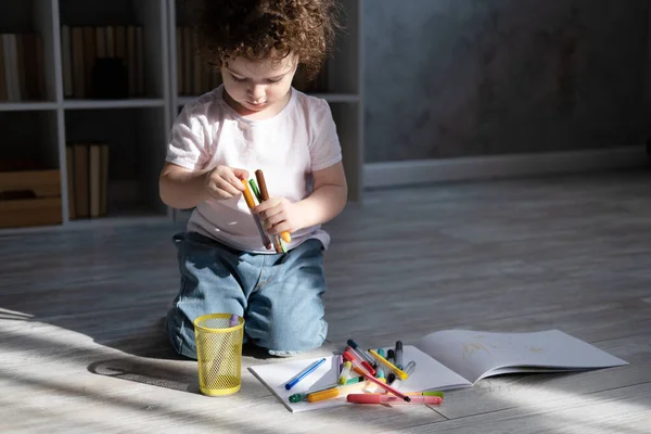 Кудрявая девочка рисует цветными маркерами, сидя на полу в гостиной дома — стоковое фото