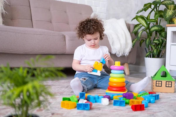 Кудрявая девочка играет с пирамидой и конструктор дома. раннее развитие детей — стоковое фото