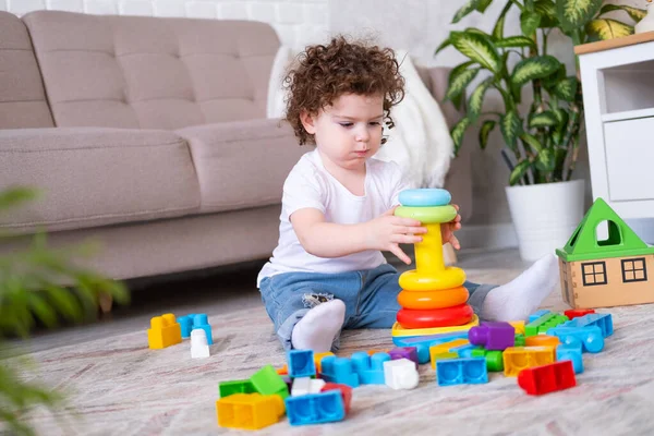 Кудрявая девочка играет с пирамидой и конструктор дома. раннее развитие детей — стоковое фото