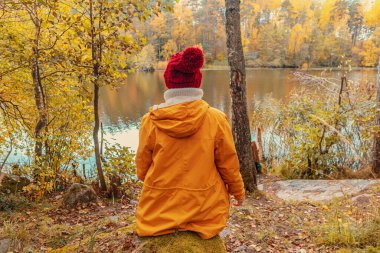 Yalnız kadın bir orman gölünün kıyısında oturuyor. Sonbahar manzarası, sakinlik, sükunet, seyahat. 