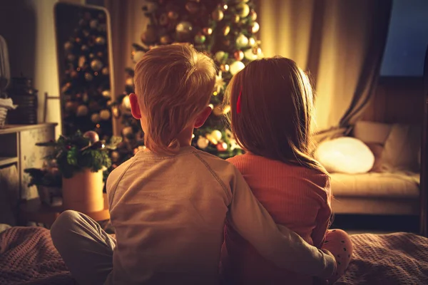 Los Niños Sientan Abrazados Cama Miran Árbol Navidad Decoraciones Navidad —  Fotos de Stock