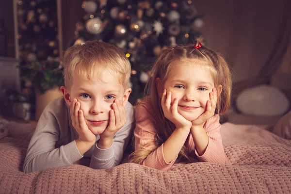 子供たちはベッドに横になってカメラを見ている クリスマスの装飾 休日を待っている — ストック写真