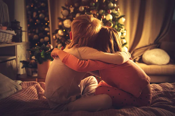 Los Niños Sientan Abrazados Cama Miran Árbol Navidad Decoraciones Navidad —  Fotos de Stock