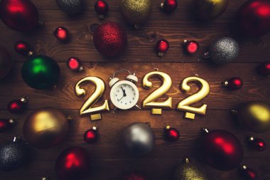 2022 numaralı mumlar, gece yarısını gösteren çalar saat, ahşap arka planda çok renkli Noel topları. Karanlık Noel geçmişi. 