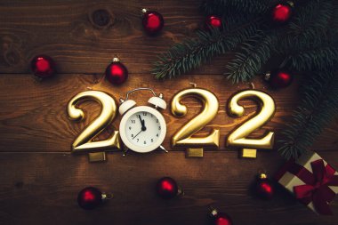 2022 numaralı mumlar, gece yarısını gösteren çalar saat, dallar, noel baloları ve ahşap arka planda bir hediye. Karanlık Noel geçmişi. 