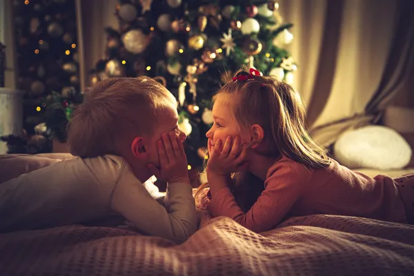 Kinderen Liggen Bed Tegen Achtergrond Van Een Kerstboom Kerstversiering Wachten — Stockfoto