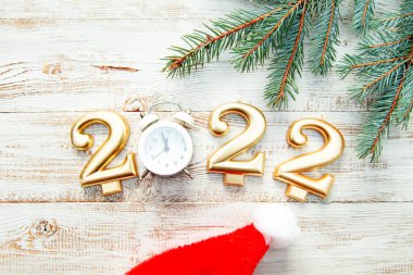 2022 numaralı mumlar, gece yarısını gösteren bir çalar saat, ahşap bir arka planda Noel ağacı dalları. Hafif Noel arkaplanı. 