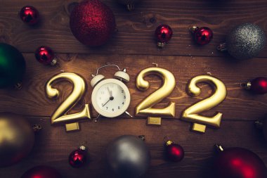 2022 numaralı mumlar, gece yarısını gösteren çalar saat, ahşap arka planda çok renkli Noel topları. Karanlık Noel geçmişi. 