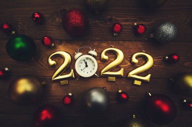 2022 numaralı mumlar, gece yarısını gösteren çalar saat, ahşap arka planda çok renkli Noel topları. Karanlık Noel geçmişi. 