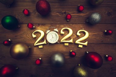 2022 numaralı mumlar, gece yarısını gösteren çalar saat, ahşap arka planda çok renkli Noel topları. Karanlık Noel geçmişi. 