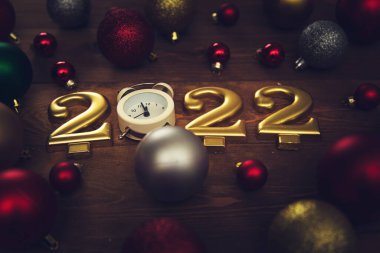 2022 numaralı mumlar, gece yarısını gösteren çalar saat, ahşap arka planda çok renkli Noel topları. Karanlık Noel geçmişi. 