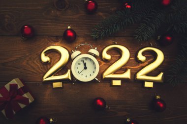 2022 numaralı mumlar, gece yarısını gösteren çalar saat, dallar, noel baloları ve ahşap arka planda bir hediye. Karanlık Noel geçmişi. 