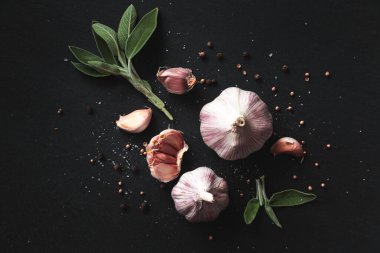 Siyah arka planda sarımsak soğanları, baharatlar, otlar ve sarımsak karanfilleri. Yakın çekim, düz yatış, üst manzara. Gıda arka planı, seçici odak. 