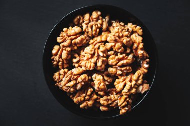 Siyah arka planda siyah bir kasede soyulmuş ceviz. Yakın çekim, düz yatış, üst manzara. Gıda arka planı, seçici odak. 