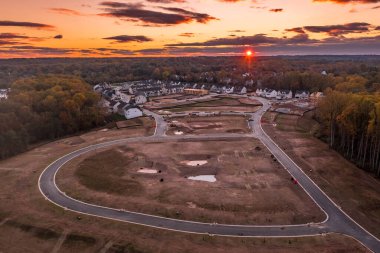 İnşaat aşamasında olan çok katlı Amerikan mahallesi sokak çemberi ve Amerika Birleşik Devletleri 'nde tek kişilik aile evleri için boş arazileri olan bir ormana kesilen sokağın ortası, gün batımı gökyüzü.