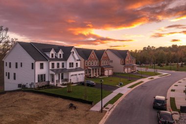 Amerika 'nın doğu kıyısında renkli dramatik günbatımı gökyüzü ile yeni inşa edilmiş bir mahalle caddesinde vinil ve tuğla cepheli yeni yalnız aile evleri.