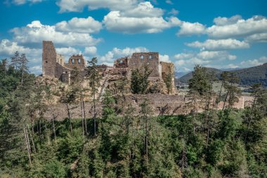 Aerial view of under restoration medieval Reviste castle above the Hron (Garam) river in Slovakia with donjon, circular gate tower, ruined gothic palace blue cloudy sky 