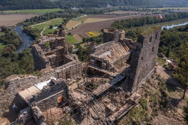 Aerial view of under restoration medieval Reviste castle above the Hron (Garam) river in Slovakia with donjon, circular gate tower, ruined gothic palace blue cloudy sky 
