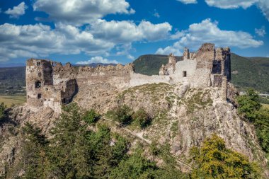 Aerial view of under restoration medieval Sasovsky castle above the Hron (Garam) river in Slovakia with circular gate tower, ruined gothic palace blue cloudy sky near Ziar nad Hronom