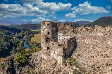 Aerial view of under restoration medieval Sasovsky castle above the Hron (Garam) river in Slovakia with circular gate tower, ruined gothic palace blue cloudy sky near Ziar nad Hronom