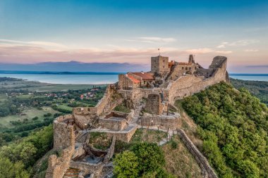 Balaton Gölü yakınındaki Szigliget Kalesi 'nin havadan görünüşü. Yeni restore edilmiş duvarları, kapı kulesi, saray binası günbatımı renkli gökyüzü.
