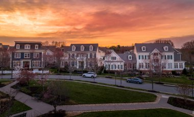 Fransız tarzı mansard çatısı ve yurt penceresi olan şık, bekar, lüks aile evleri, beyaz bahçe çitleri, çok arabalı malikaneler Maryland 'de, Amerika Birleşik Devletleri' nin gün batımı gökyüzünde yeni bir yerleşim yeri olan emlak camiasında.