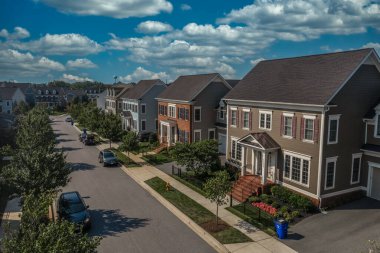 Aerial view of modern upper class suburban American real estate development community, large single family homes with vinyl and brick siding portico leading up to the entrance cloudy blue sky clipart