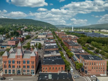 Aerial view of Corning Steuben County, New York downtown, Market Street, glass factory, chemung river, centerway walking bridge, little joe tower, parking lot with cloudy blue sky