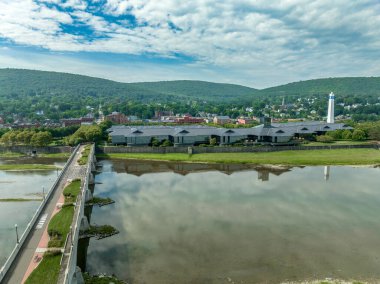 Aerial view of Corning Steuben County, New York downtown, Market Street, glass factory, chemung river, centerway walking bridge, little joe tower, parking lot with cloudy blue sky