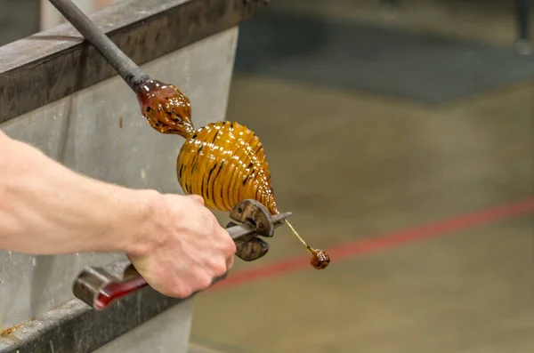 A female hand of a Glass Blower cutting molten colorful glass into a  colorful piece