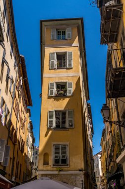 Sarı duvarlı düz demir bina, hoş eski kasabada yeşil ahşap panjurlu pencereler.